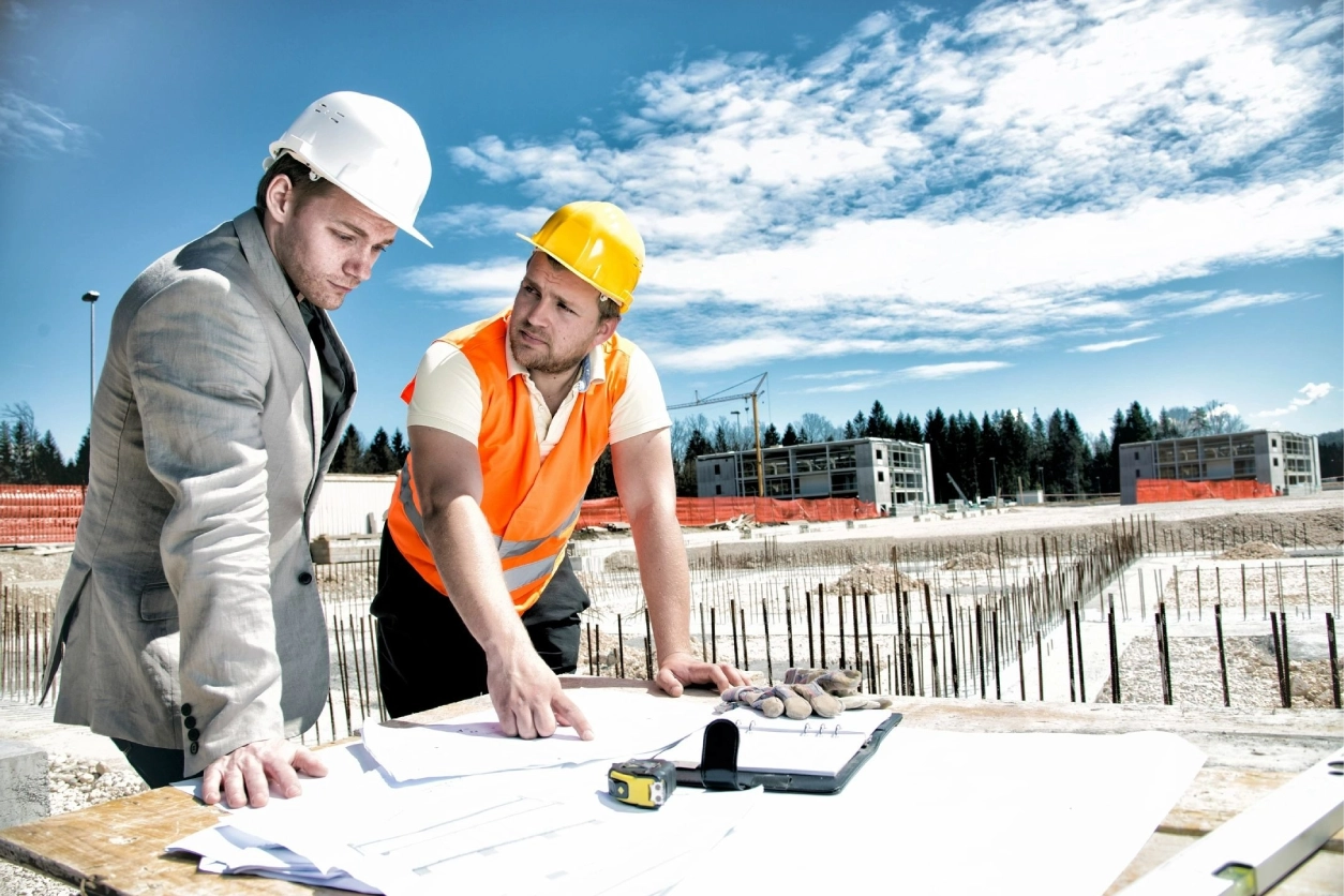Two men in hard hats looking at plans on a table.