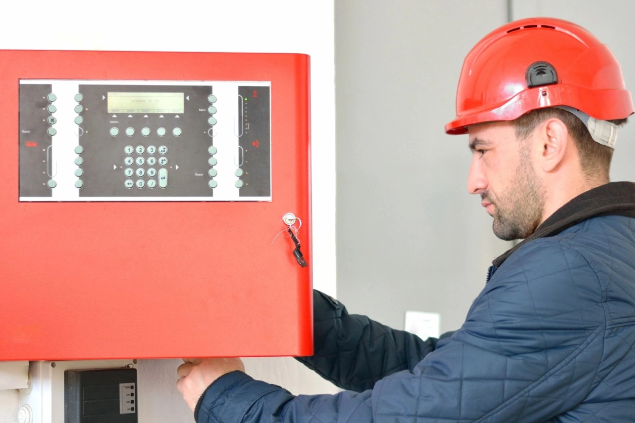 A man in red helmet holding up a fire alarm.